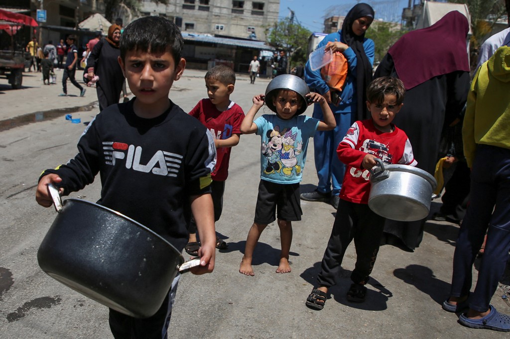 Palestinian children wait to receive food cooked by a charity kitchen, amid a desperate shortage of aid supplies