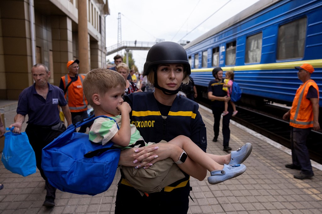 An emergency service worker carries a child at a train station amid the evacuations